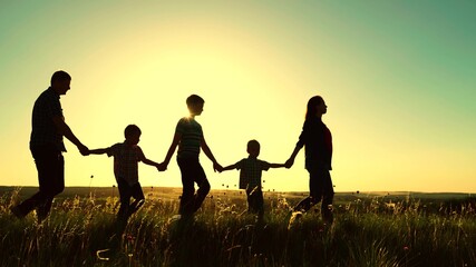 Naklejka na ściany i meble Happy family team with children walking together holding hands in the summer park. Children, sons, hold mom and dad by the hand. Teamwork of people. A group of people of different ages at sunset.