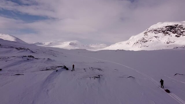 A tiny skier and snowshoeing drone pilot on a skiing Kungsleden trail between Alesjaure and Tjaktja mountain huts, April, Lapland, Sweden