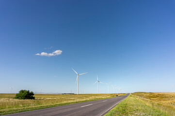 Asphalt path to the horizon surrounded by electricity generating windmills. Blue sky with a single...