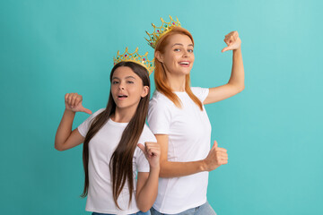 Happy woman and girl kid in crowns point fingers at promotional tshirts for copy space, advert
