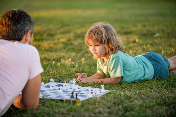 happy family of parent and child playing chess on green grass in park outdoor, family relations.
