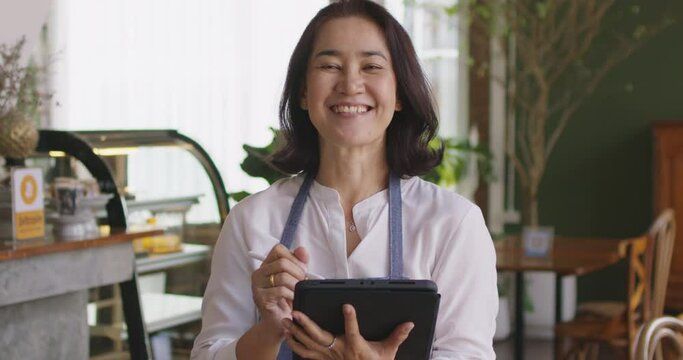 Mature adult asia people open small bar pub look at camera enjoy laugh work with pride stand at modern SME store. Casual apron chef clerk staff use online order in food and drink cafe coffee shop app.