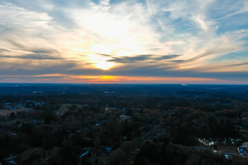 Fototapeta na wymiar a stunning aerial shot of a radiant sunset with blue sky and powerful clouds with vast miles of lush green and autumn colored trees with homes nestled in the trees in Powder Springs Georgia USA