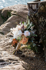 wedding bouquet of white and orange flowers resting against tree stump at the edge of a lake