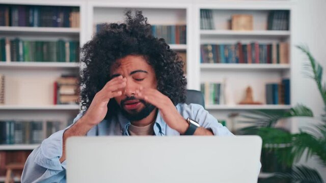 Troubled young Arabian man reading bad news in message with puzzled emotions at laptop screen at office table. Stressed male looking at screen, touching face confused by computer problem or crash.
