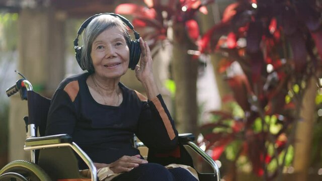 Asian senior woman listening music with headphone in backyard..Asian senior woman listening music with headphone in backyard