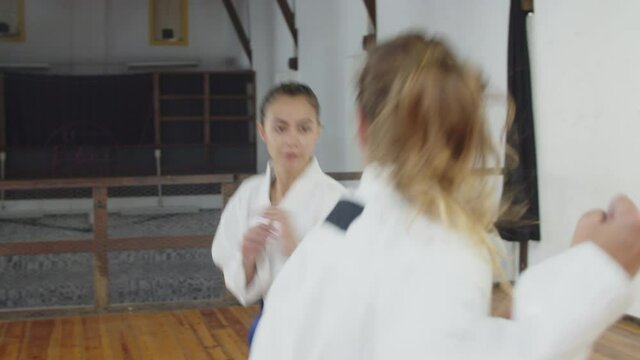 Handheld shot of girls bowing before starting karate training. Medium shot of focused Caucasian teenagers in kimonos having karate lesson in gym, doing physical activity. Martial arts, sport concept