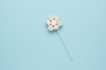 Multicolored marshmallow on a stick on a blue background.