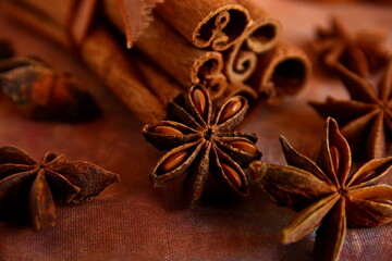Macro heap of star anise and group sticks of cinnamon on brown background of canvas fabric. Selective focus