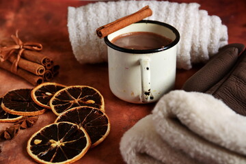 Winter warming drink hot chocolate with foam and cinnamon sticks in tin bowl, woman gloves and white down knitted scarf on table decorated with spices, star anise, slice of dry lemon