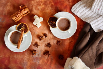 Winter warming drink hot chocolate with foam and woman gloves and white down knitted scarf. Top view on table decorated with spices, cinnamon sticks and star anise, slice of lemon and heap sugar