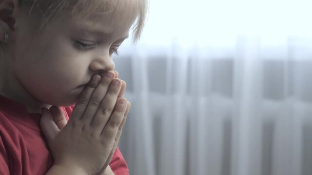 little daughter girl makes a wish prayers bedtime religion concept . prayer child indoors praying by bed lifestyle front of window