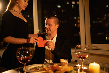Romantic dinner for Valentine's Day for two, a date with a candle with wine in the evening, a couple in love, a girl giving a man a heart