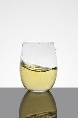 crystal glass with moving white wine making waves and white background