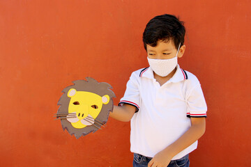 Latin little boy in uniform shirt proudly and happily shows the lion mask he made for school...