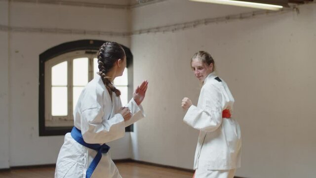 Tracking shot of focused girls having karate class in gym. Medium shot of concentrated teenagers training together, doing physical activity, devoting time to hobby. Martial arts, sport concept