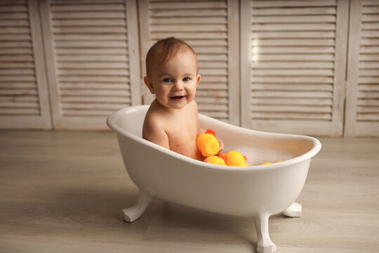 a baby of 11 months is bathing in a white baby bath with rubber ducklings, the baby is laughing, the concept of children's goods. high-quality photography