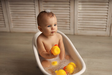 a baby of 11 months is bathing in a white baby bath with rubber ducklings, the baby is laughing, the concept of children's goods. high-quality photography