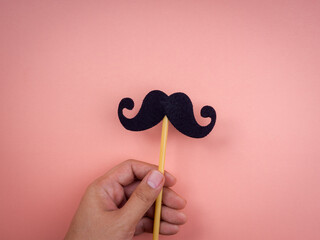 Hand holding and showing mustache stick isolated on pink pastel background, minimal style. Happy fathers day, Movember concept.