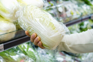In the supermarket a male hand holds a Chinese cabbage close-up.
