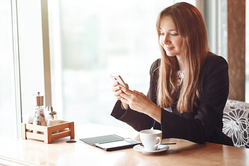 Young business woman using her smart phone and smiling in coffee shop