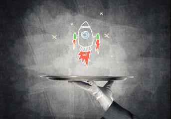 Hand of waiter presenting sketched rocket on tray