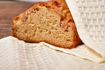 Sliced freshly baked homemade apple pie, covered with a beige napkin, towel on a brown wooden table. Homemade cakes - apple charlotte. Close-up, a place to copy