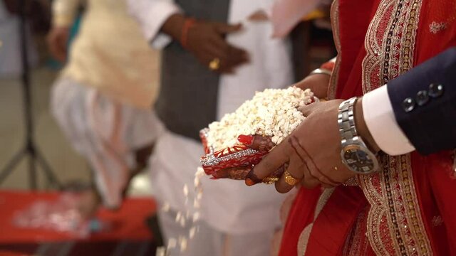 Cinematic shot of a Hindu couple throwing puffed rice (khoi daan) in fire in presence of brahmin during a traditional Hindu wedding in India