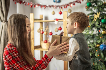 Happy mom and child near the Christmas tree are giving gifts and smiling. Concept of New Year mood, festive atmosphere
