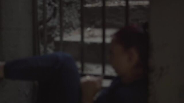A frustrated, trapped woman pounds her face and the prison walls in an ancient stone room with a steel bar window grill.