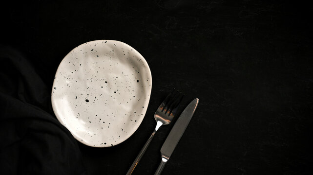 Minimal handmade ceramic plate with modern cutlery on a black table