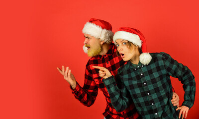 Christmas party. Idea for fun. Good mood. Winter joy. Couple in love pointing copy space. Look at this. Santa Claus style. Christmas time. Man and woman christmas holiday celebration. Family shopping