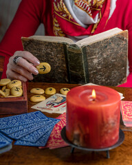 A fortune teller dressed in red reads cards and an ancient book to predict the future