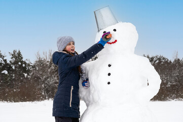 Cute girl makes  snowman on  winter day. Girl on a snow-covered field in the open air. Active...