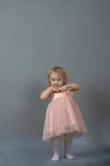 Cute baby girl 2 years old caucasian dancing in pink prom dress on a gray background in the studio