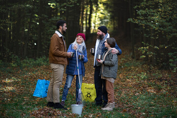 Diverse group of happy volunteers cleaning up forest, having break, drinking tea and talk together.
