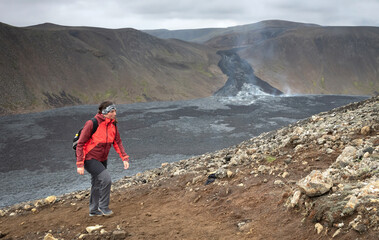 Fototapeta premium Woman walking near the new lavafield of the volcano eruption at Fagradalsfjall