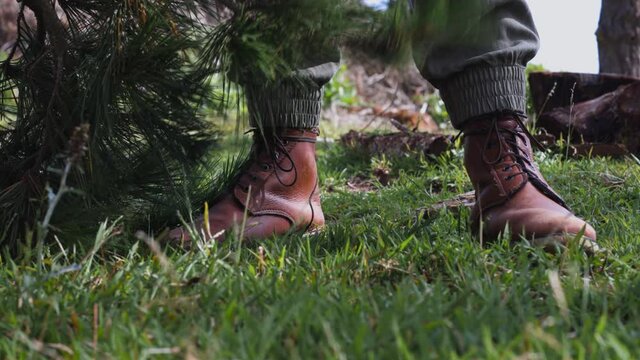 Woman picking up small pine tree, revealing her leather shoes, and places axe on ground.