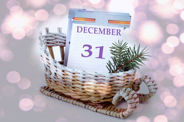 Calendar for December 31: leaves of a calendar with the name of the month, number 31 in a decorative sleigh, a fir branch on a light background, close-up