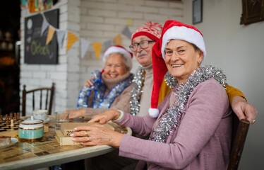 Happy senior friends sitting indoors in community center and celebrating Christmas.