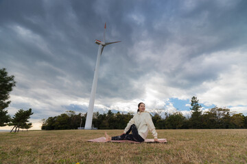 風力発電機がある公園でヨガを練習している若い女性