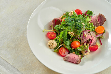 Salad with roast beef and pine nuts in a white plate.