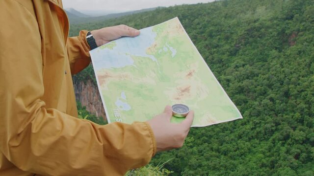 Compass and map in hands of traveler for checking and searching position and direction at the top of peak of mountain while hiking for camping