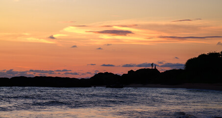 Silhouetted people on the rocky beach in the paradise island of Sri Lanka. The spectacular evening sky and the calm ocean waves create a romantic evening vibe.