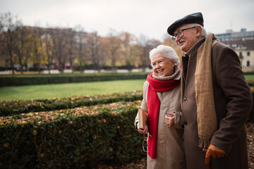 Happy senior friends on walk outdoors in town park in autumn, holding and laughing.