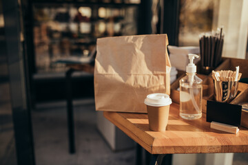 Takeaway food in paper bag and coffee to go on table near restaurant window. Social distancing during quarantine caused pandemic.