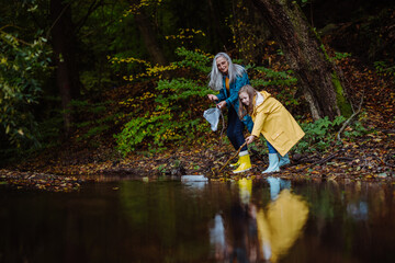 Small girl with grandmother picking up waste from little lake outoors in forest.