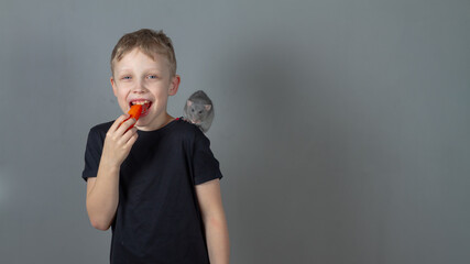 Cheerful caucasian boy eats healthy food vegetables carrots with a pet gray rat in the studio