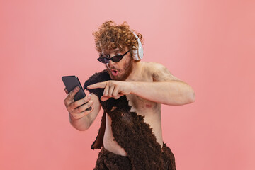 Cropped portrait of man in character of neanderthal using phone and listening to music in...
