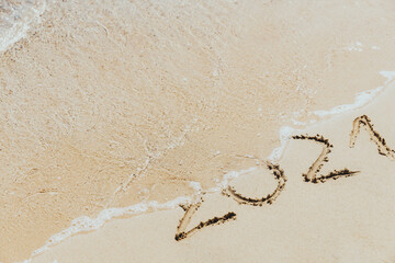 Waves wash away the inscription on the sand 2021. Concept of the outgoing year
